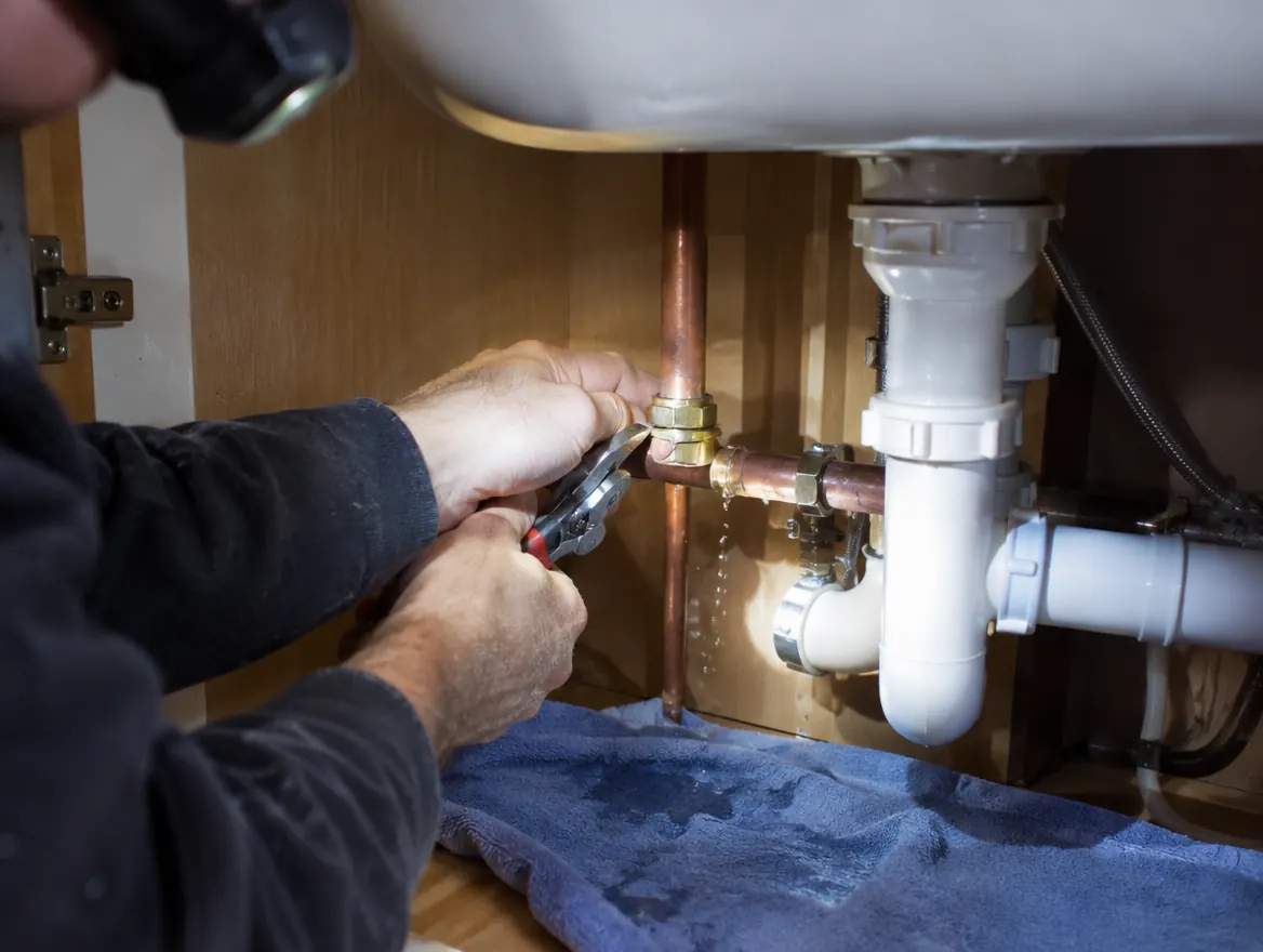 Plumber tightening a fitting on a leaking pipe under a sink